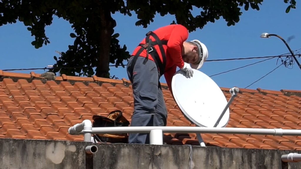 Homem instalando parabólica digital no telhado de uma residência