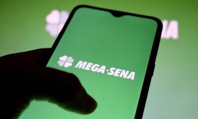 Mega-Sena mão segurando celular com logo das Loterias