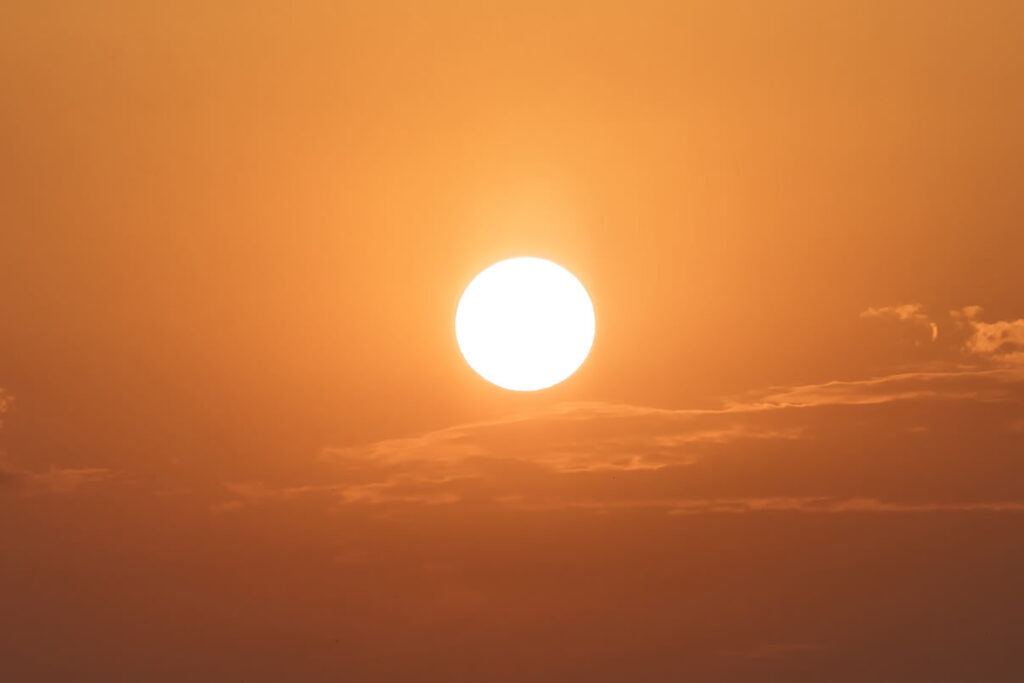 Foto exibe céu avermelhado com sol entre nuvens